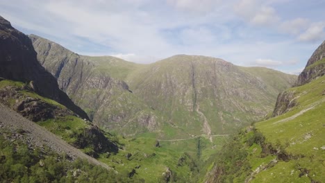 green meadow on the foreground with the three sisters mountains in the background and a giant valley underneath, glencoe scotland on a partly cloudy day