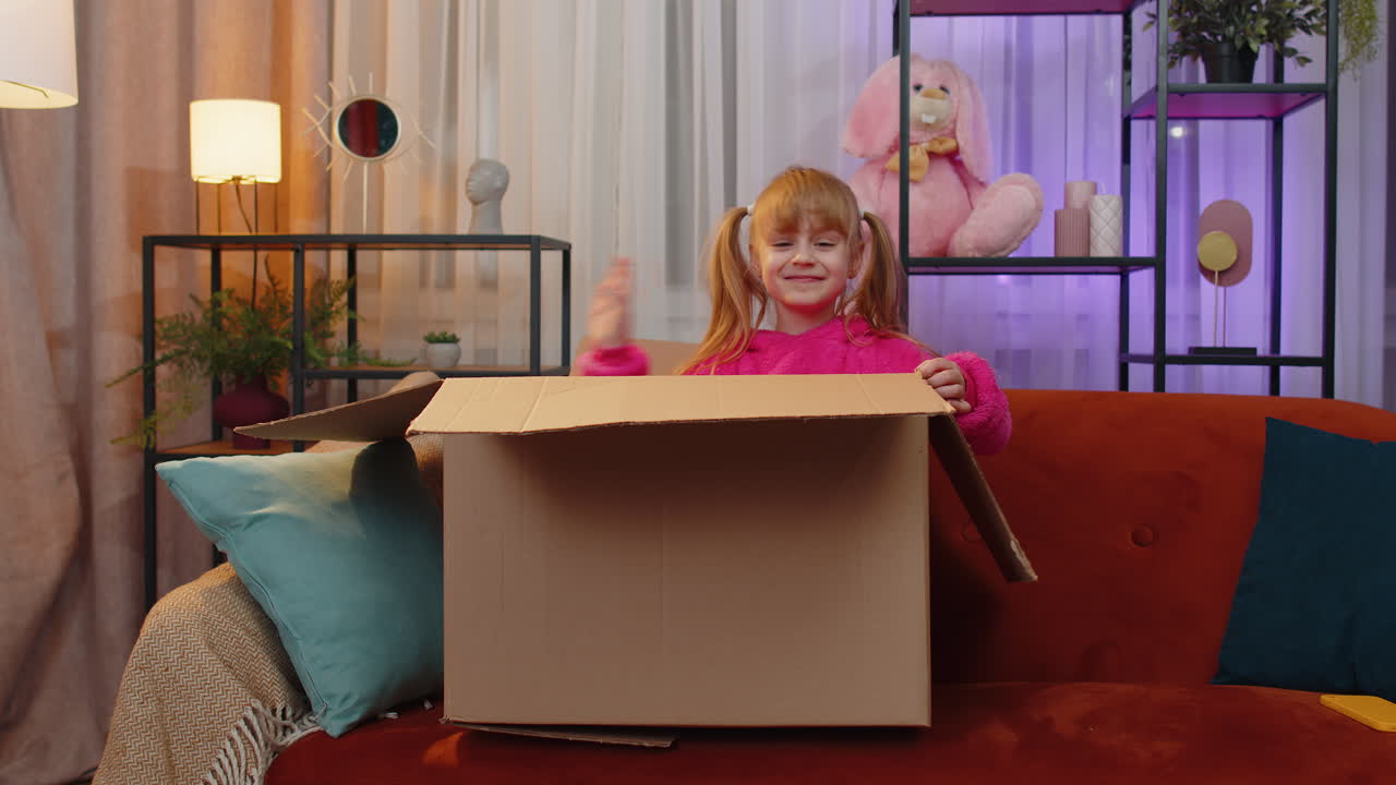 una niña feliz juega al escondite saltando de una caja de cartón riendo escondiéndose dentro del paquete