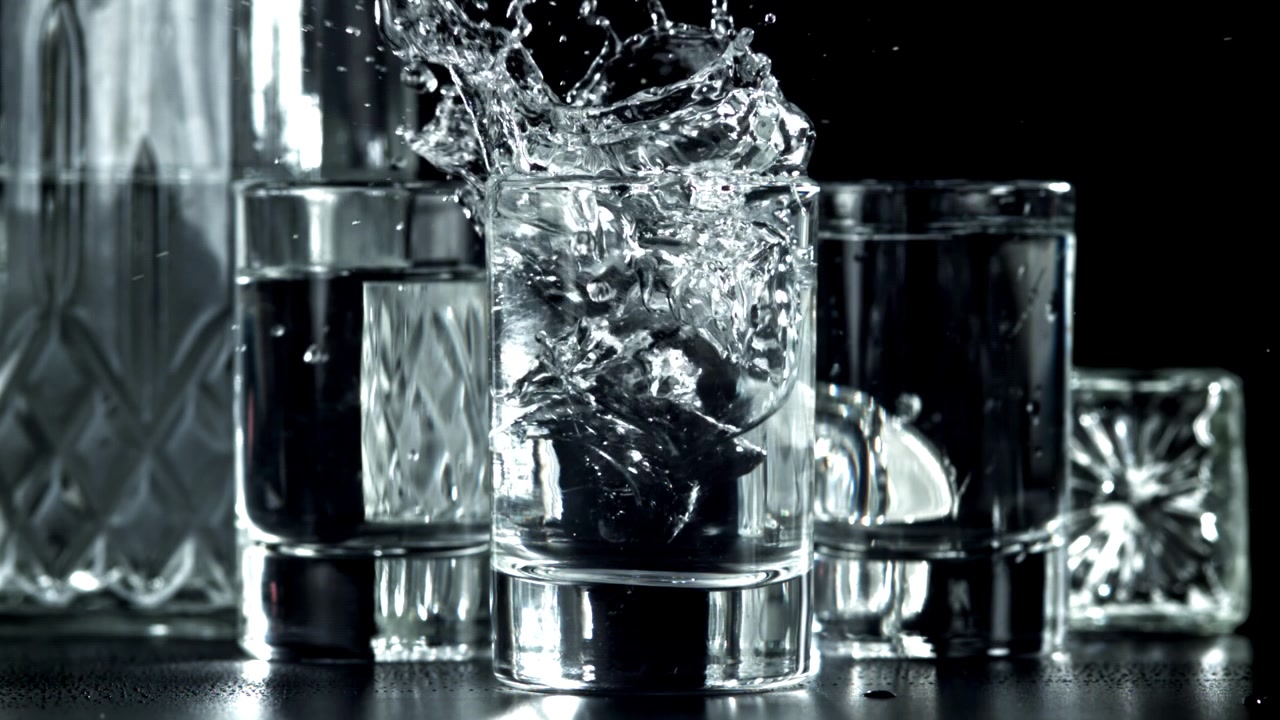 Cubetti di ghiaccio che si tuffano in un bicchiere di liquido trasparente al rallentatore