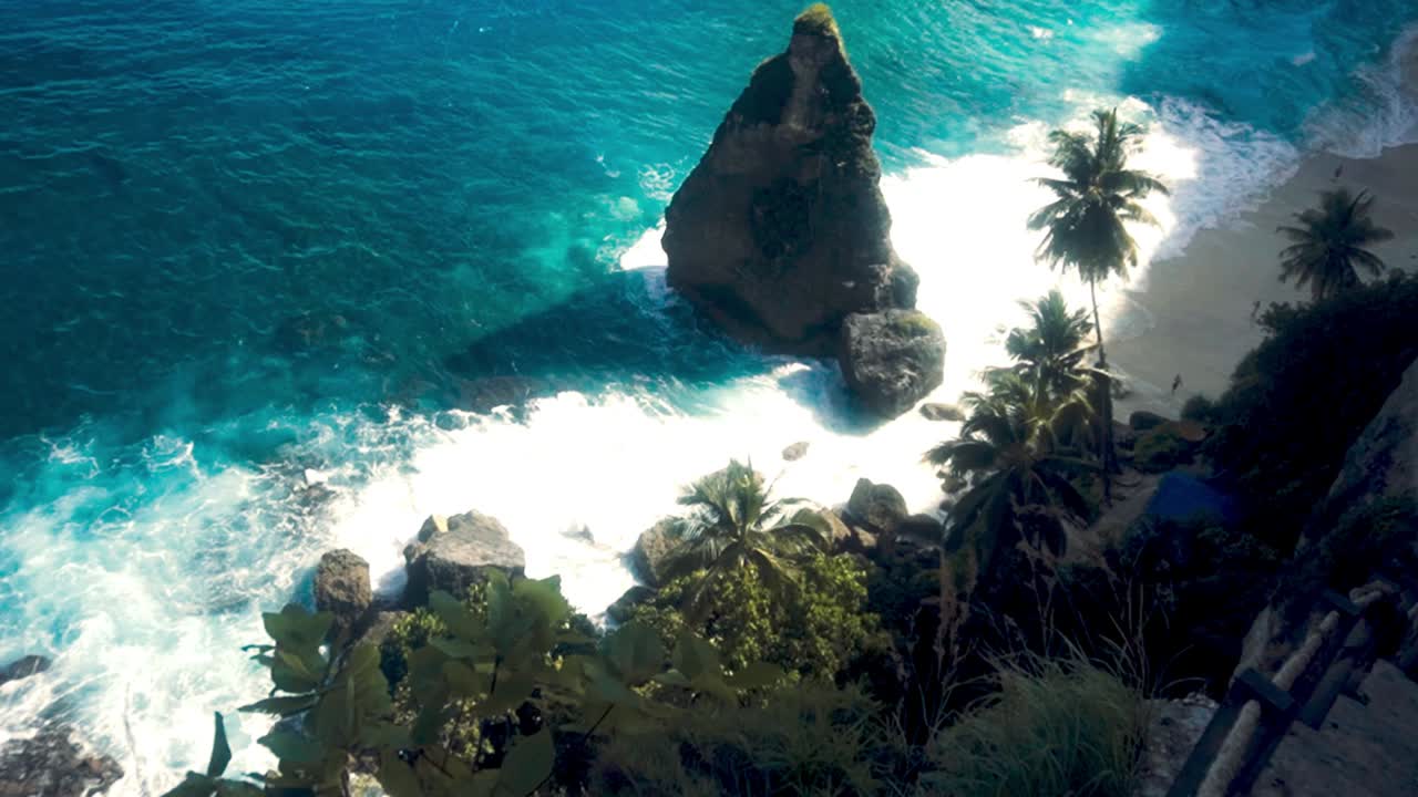 Panoramatický záběr turisty na římse vysokého skalnatého útesu poblíž pláže s čistou modrou vodou na Bali za slunečného dne.