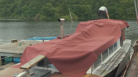 young man securing waterproof canvas cover over wooden boat