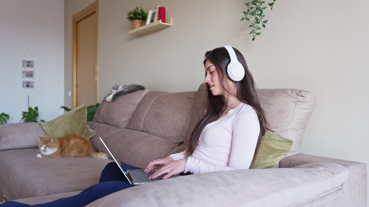 Giovane donna con le cuffie che usa il laptop sul divano a casa