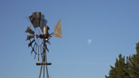 viejo molino girando con el viento, con la luna en un cielo azul, en patagonia, argentina