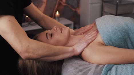 portrait of a pretty dark-skinned woman lying on a massage table having a clavicle massage by male hands