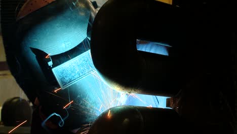 reverse close-up zooming out shot of a welder in full protective hse kit welding pipes at a factory with intense light and nice sparks from the welding operation