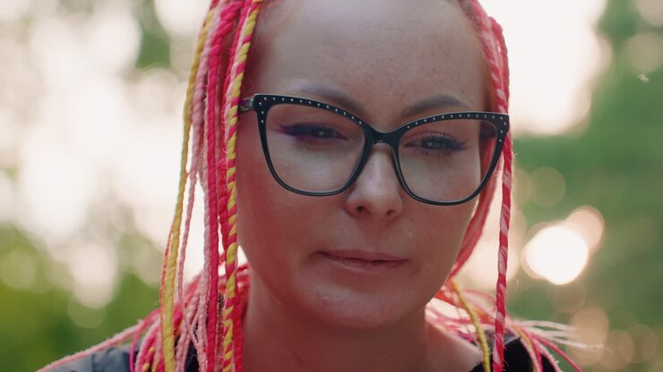 lady with colorful plaits observes tranquility, serene woman with glasses enjoys peaceful park moments, gentlewoman donning vivid braids and spectacles gazes downward amid quiet park surroundings