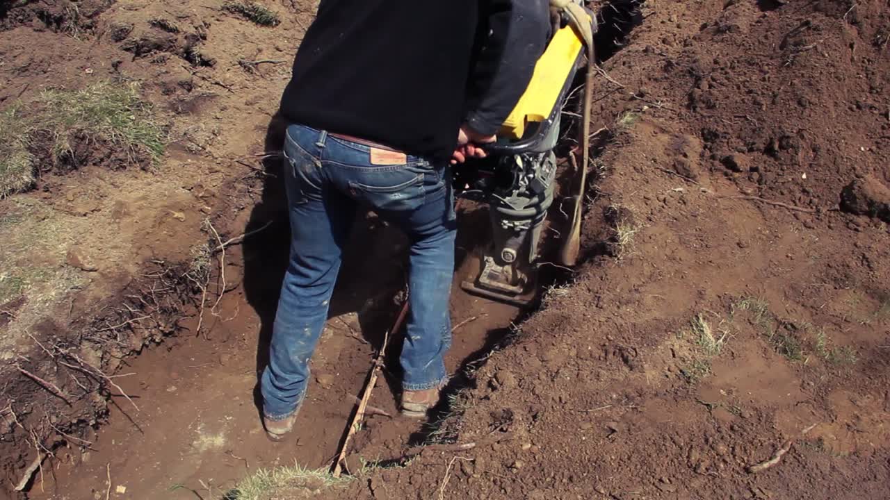 A worker compacts dirt in a trench