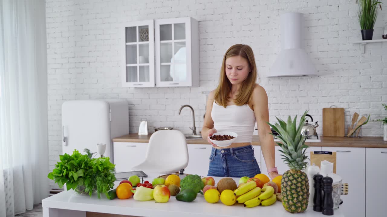 Pretty woman in the modern kitchen. Organic fruit and vegetables on the table. Young woman eating vegan food. Healthy diet concept.