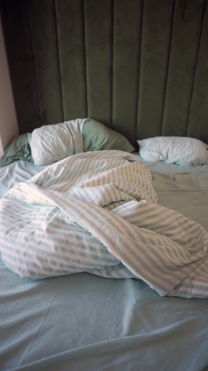 Tempat Tidur yang Belum Dirapikan dengan Selimut Bergaris dan Sandaran Kepala Hijau