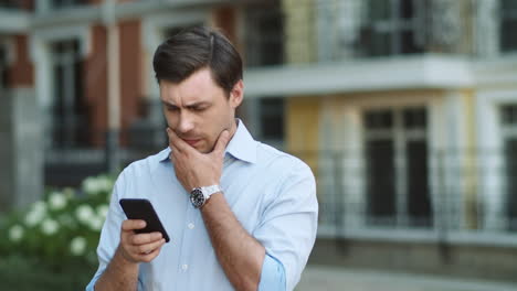 Closeup-businessman-reading-serious-news-on-phone.-Man-typing-on-phone-at-street