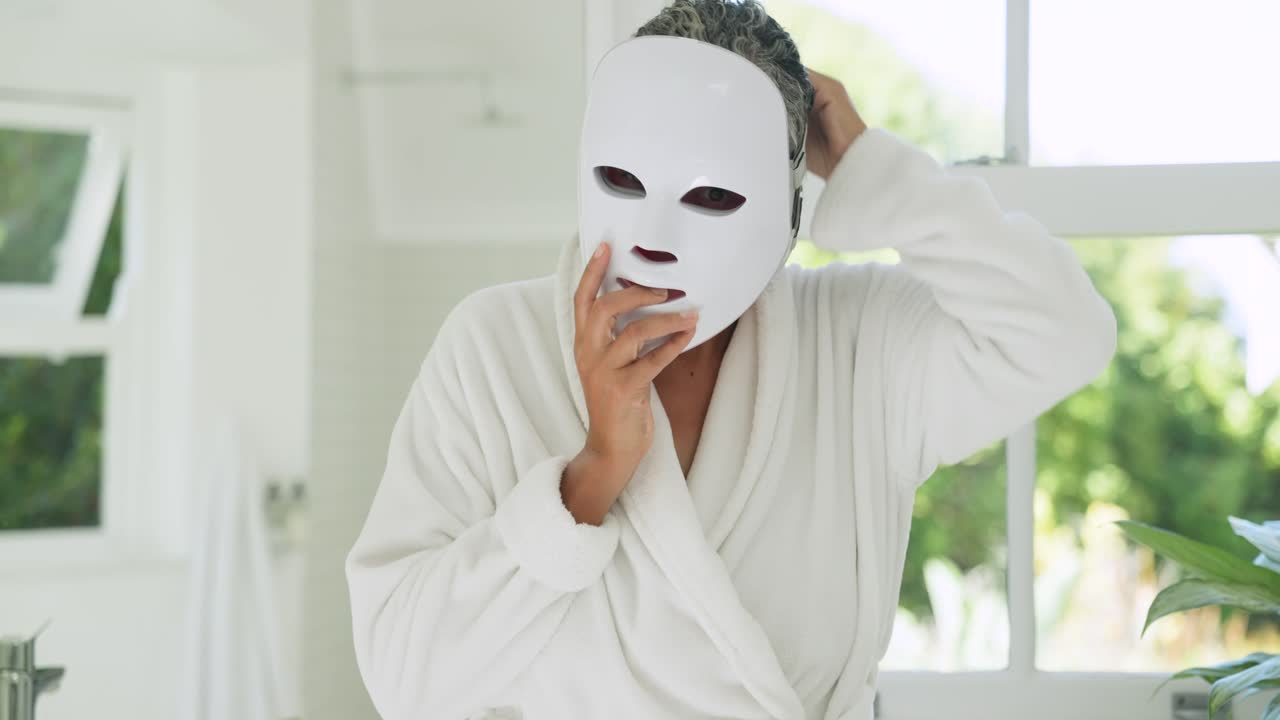 Eine ältere Frau im Bademantel nimmt eine weiße Maske von der Ablage am Waschbecken im Badezimmer und bereitet die Maske für die Hautpflege vor.