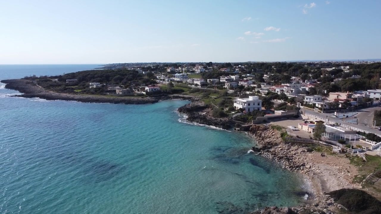 Ripresa aerea con drone di una città costiera imbiancata a calce lungo la costa rocciosa con acqua turchese mediterranea, paesaggio marino panoramico che mostra l'architettura e la bellezza naturale della Costiera Amalfitana, Italia