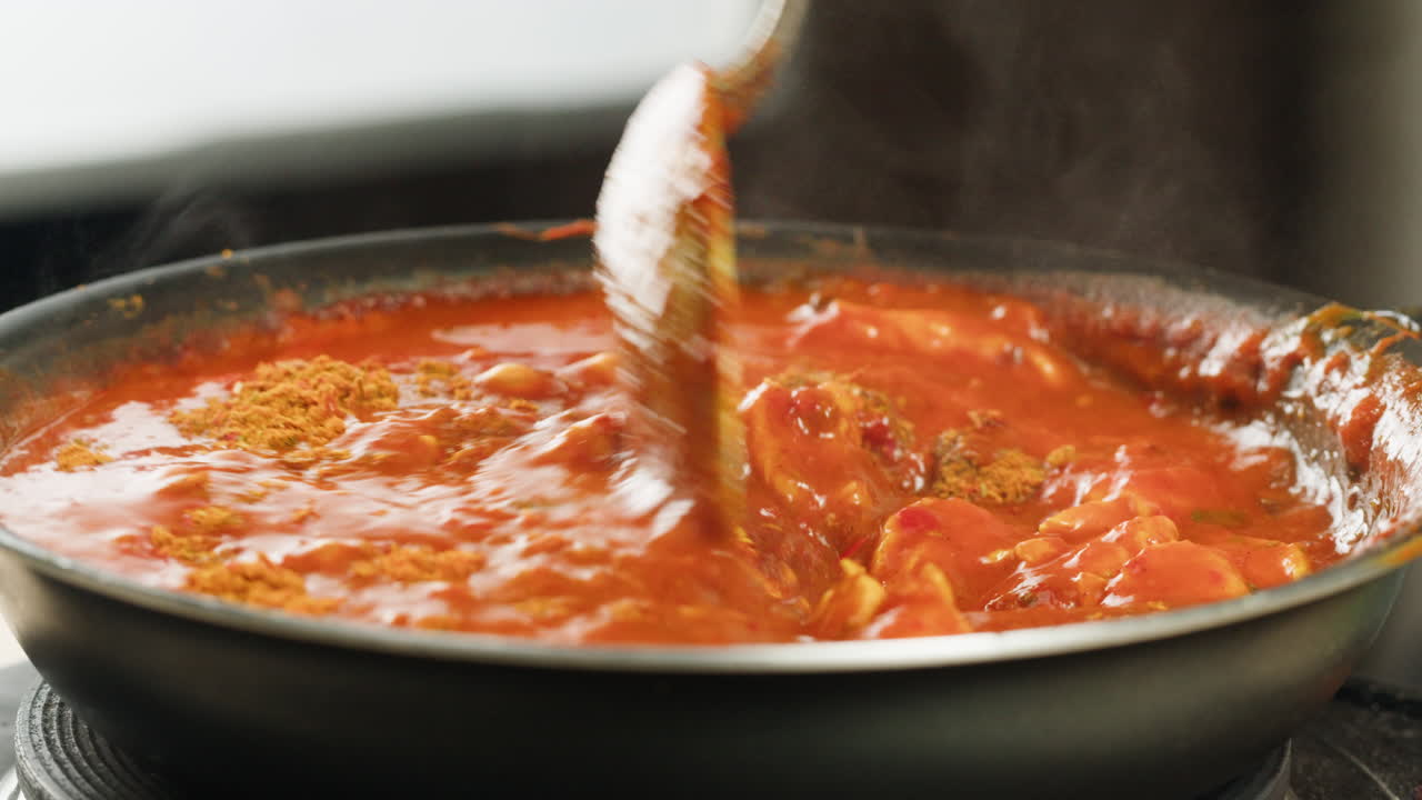 Chicken in tomato sauce is boiling on a frying pan with spices. Cooking tomato sauce curry with chicken fillet. Traditional Italian Mexican Asian dish. High quality studio shot for cafe, restaurant close up.