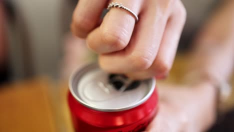 A close-up view of a person’s hand opening a red aluminum can, with natural lighting, shallow depth of field, and steady camera focus