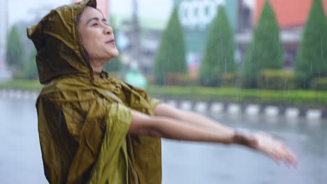 an asian girl with positive face expression on the pouring rain day, standing on the road side wearing yellow raincoat soaking wet in the rain, its rainy season in asia, enjoying her day with rain