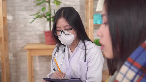 doctor of asian appearance in a protective medical mask communicates with a sick asian woman in the living room close up