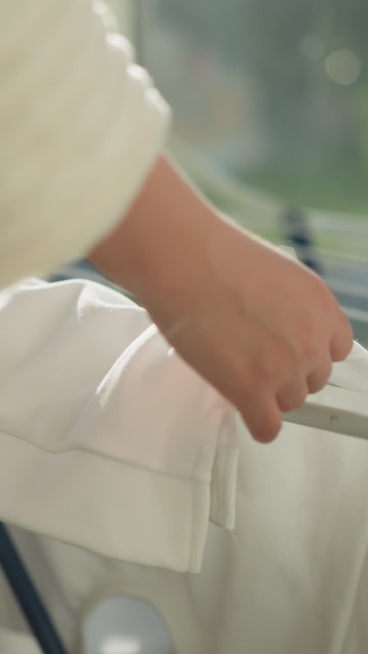 여성은 발코니에 옷 건조기에 옷을 매달고, 여성은 현대적인 평평한 느린 동작으로 빛 발코니에서 건조판에 매달린 옷을 는다.