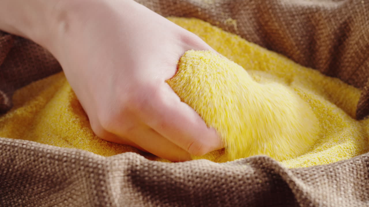 Close-up of a hand sifting corn grits or cornmeal in a burlap sack