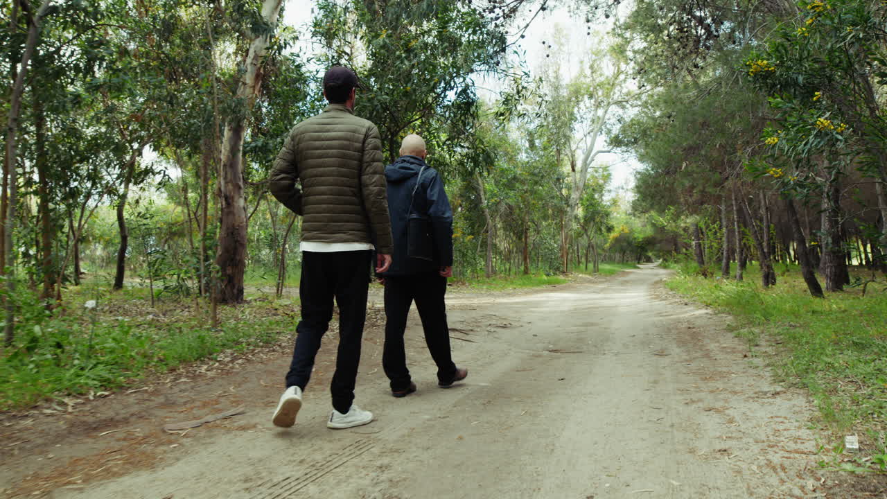 Young Boy Walks With Elderly Man On Park Path During Father's Day