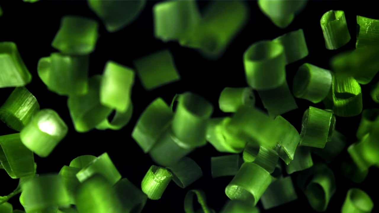 Vibrant Green Onion Pieces Falling Against a Dark Background