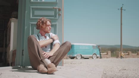 man sitting by a door, vintage van in the background