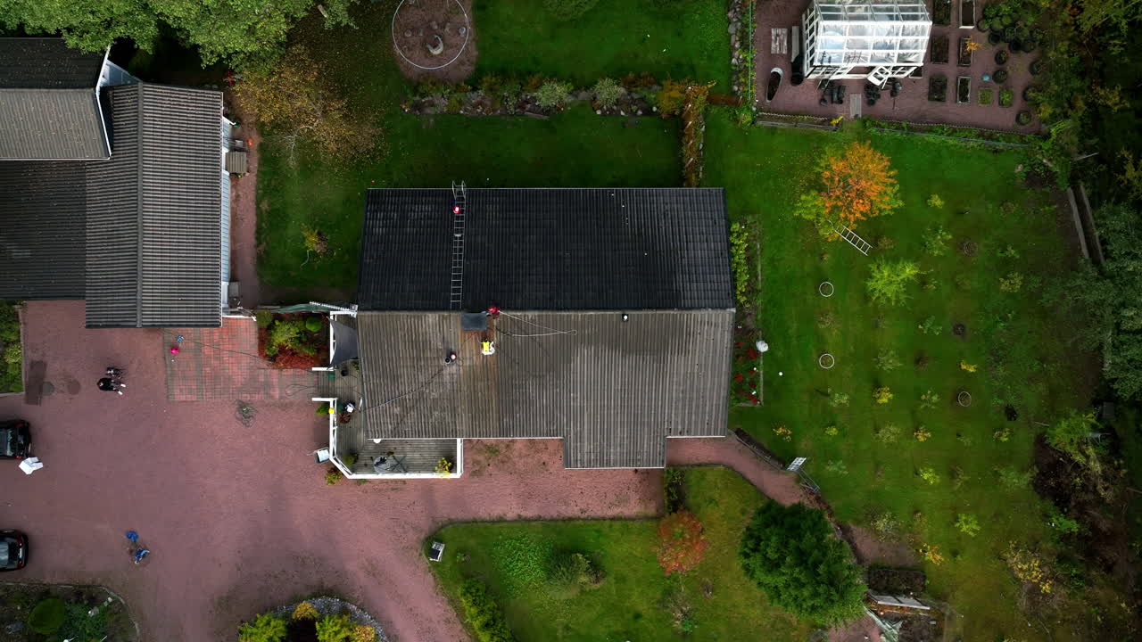 Cenital drone shot rising above a worker washing moss and dirt from a house roof