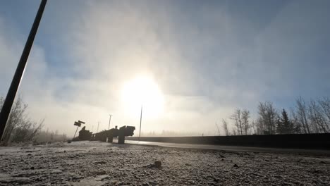 video loop time lapse 4k transportation of a dual compressed gas white fuel truck on a twilight winter day with snow covered forest as the fog subsides on sunny sunrise day