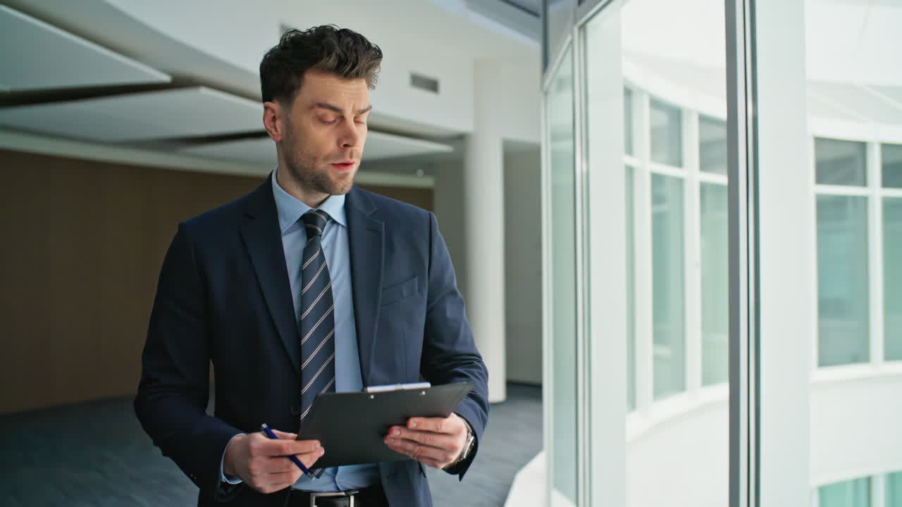 Focused businessman reading clipboard walking hallway closeup. Serious executive