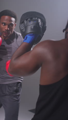 vertical video studio shot of male boxer sparring working out with trainer wearing punch mitts or gloves practising for fight 5