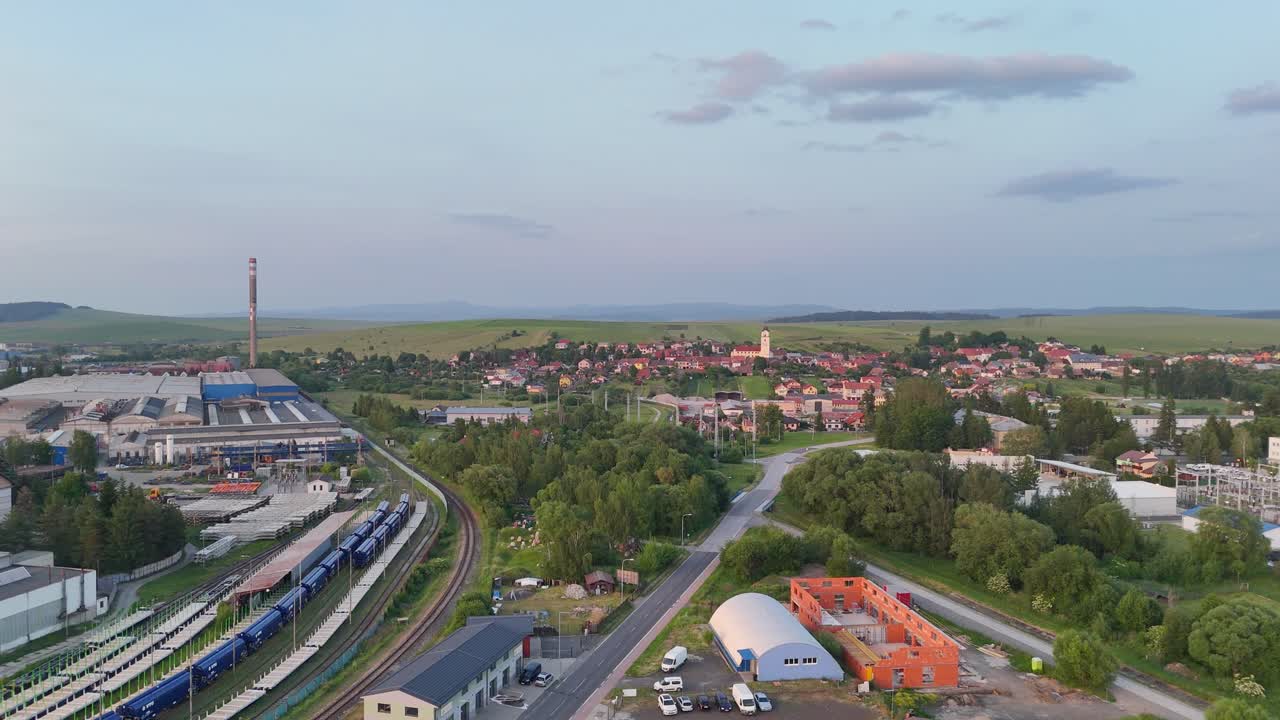 Drone rising and flying backward over Poprad industrial area with nearby residential houses and open countryside in the background
