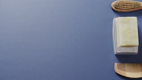 Close-up-of-soap,-brush-and-comb-on-blue-background-with-copy-space