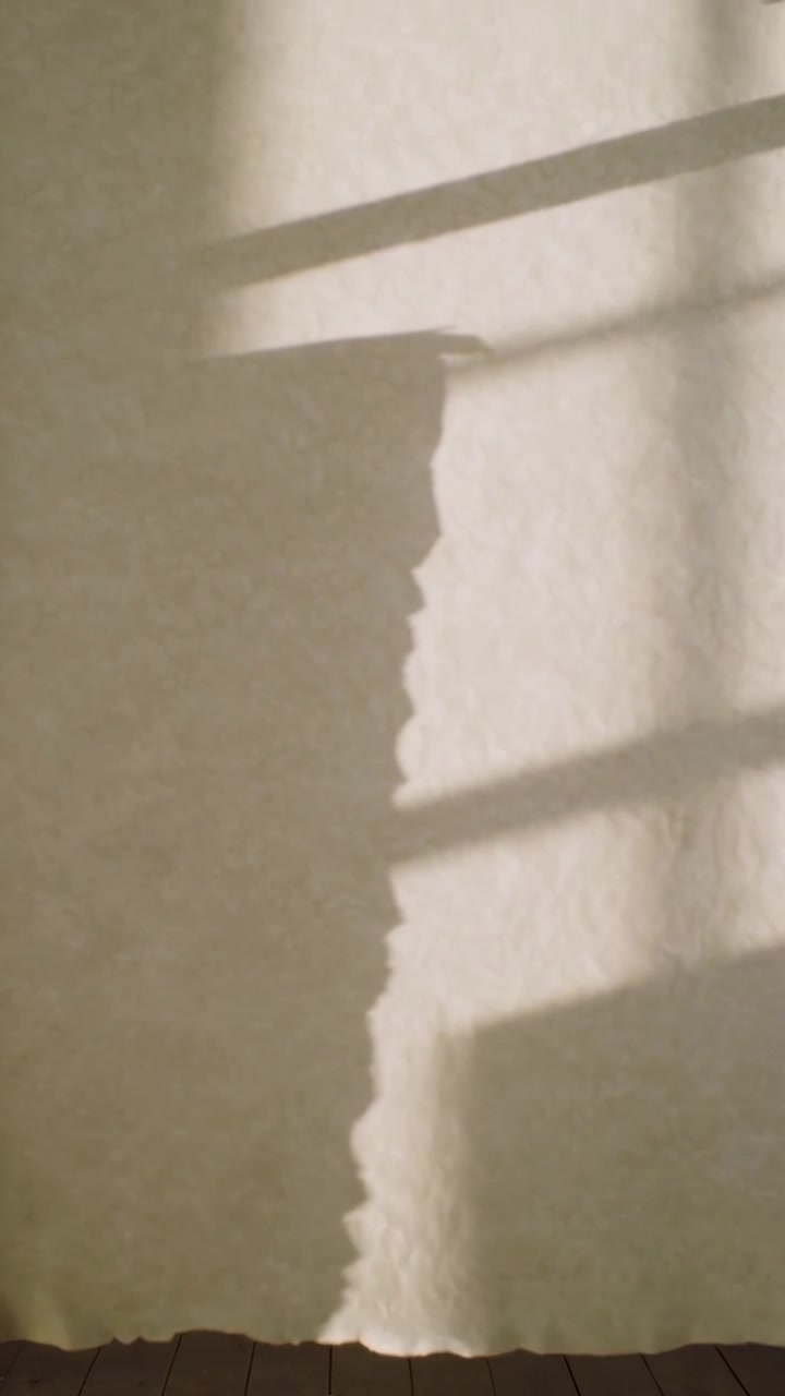 Vertical video: Shifting light revealing profile moving behind white sheet on deck, slatted shadows