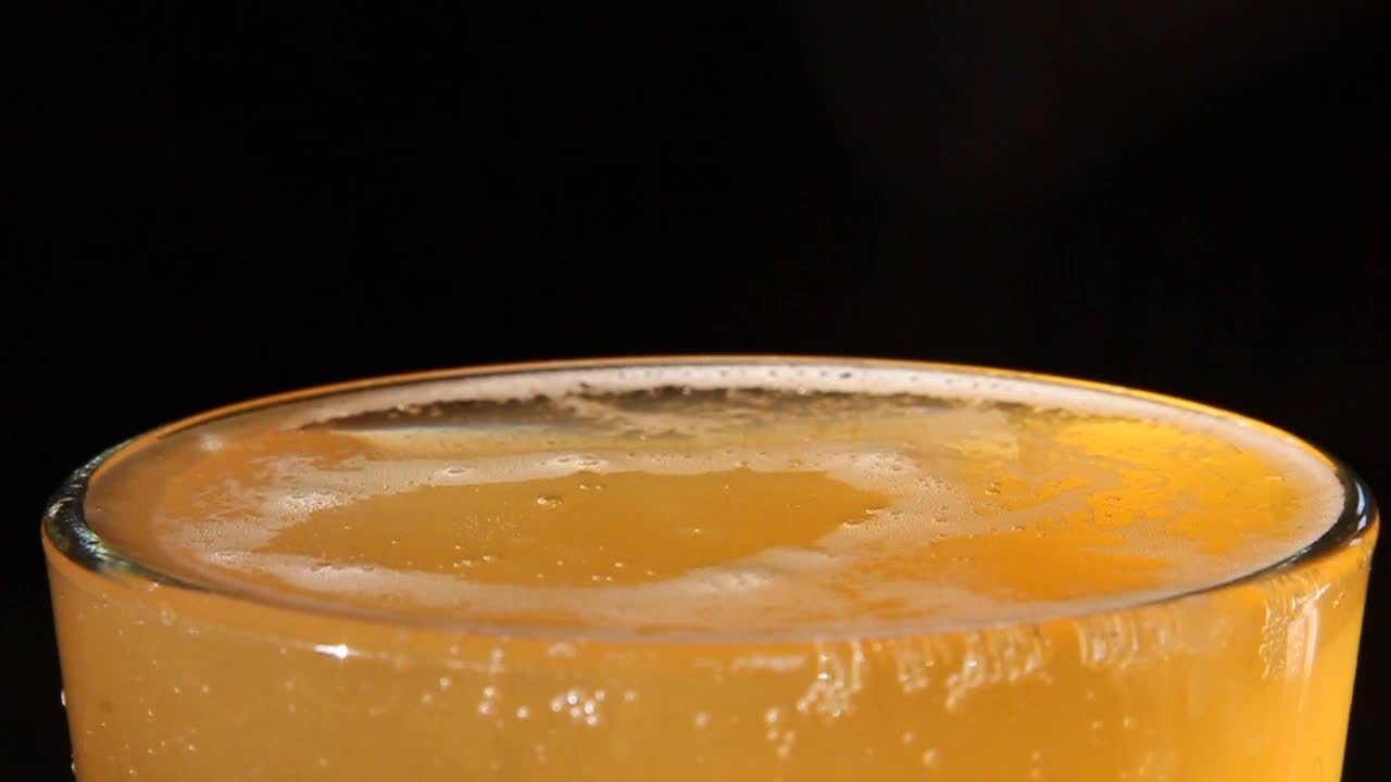 Un bicchiere alto di birra rinfrescante con una singola goccia che vi cade dentro, creando un'elegante increspatura sulla superficie