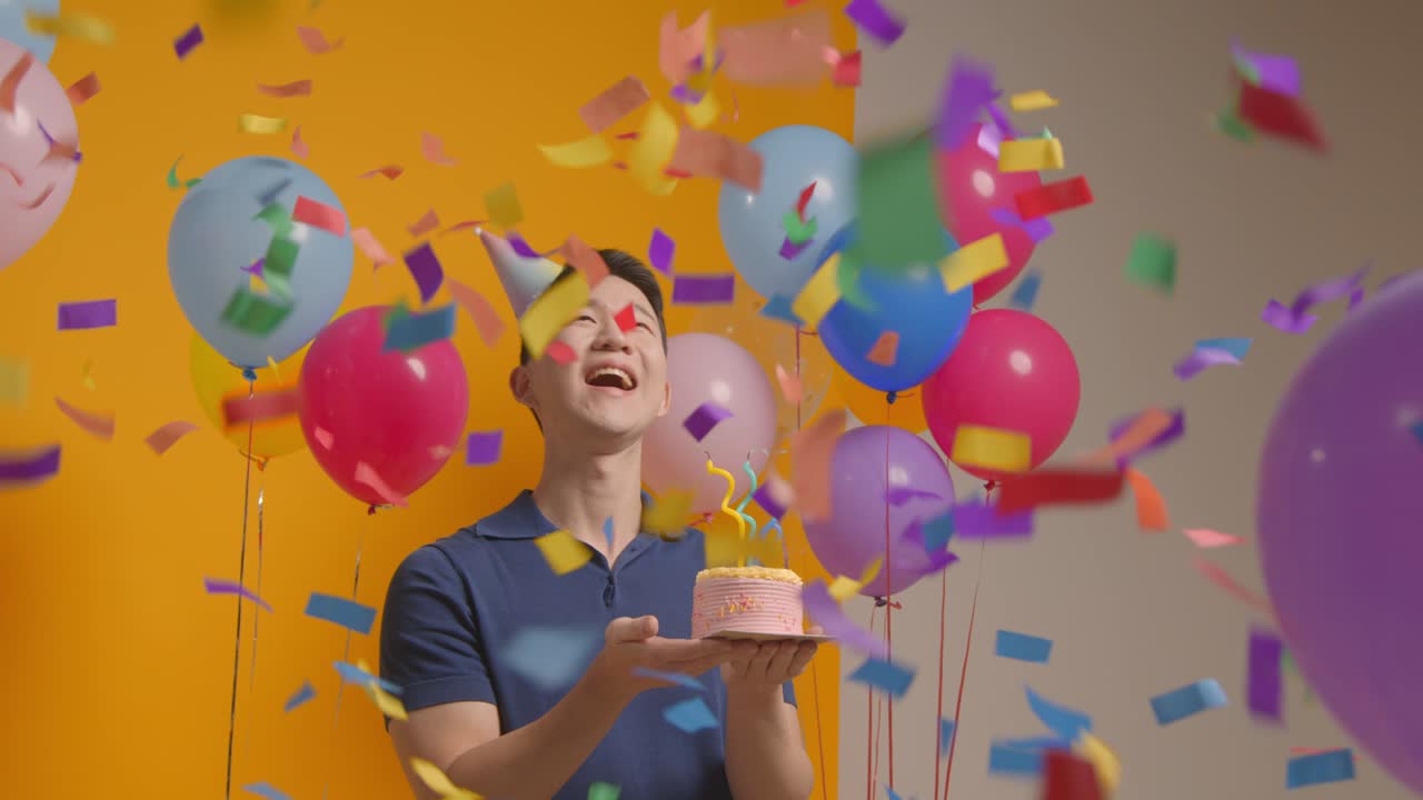 retrato de estudio de un hombre con un sombrero de fiesta celebrando su cumpleaños soplando velas en un pastel con confeti de papel