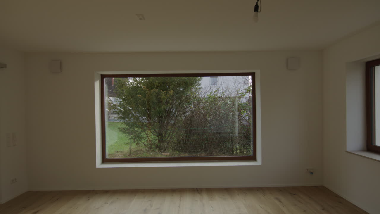 Toma de seguimiento lenta en un salón recién renovado, mirando una enorme ventana orientada al sur. Gran viga y horno visibles