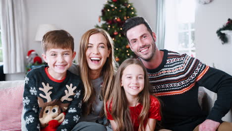 retrato de padres con niños con suéteres festivos sentados en el sofá en la sala de estar en casa el día de navidad