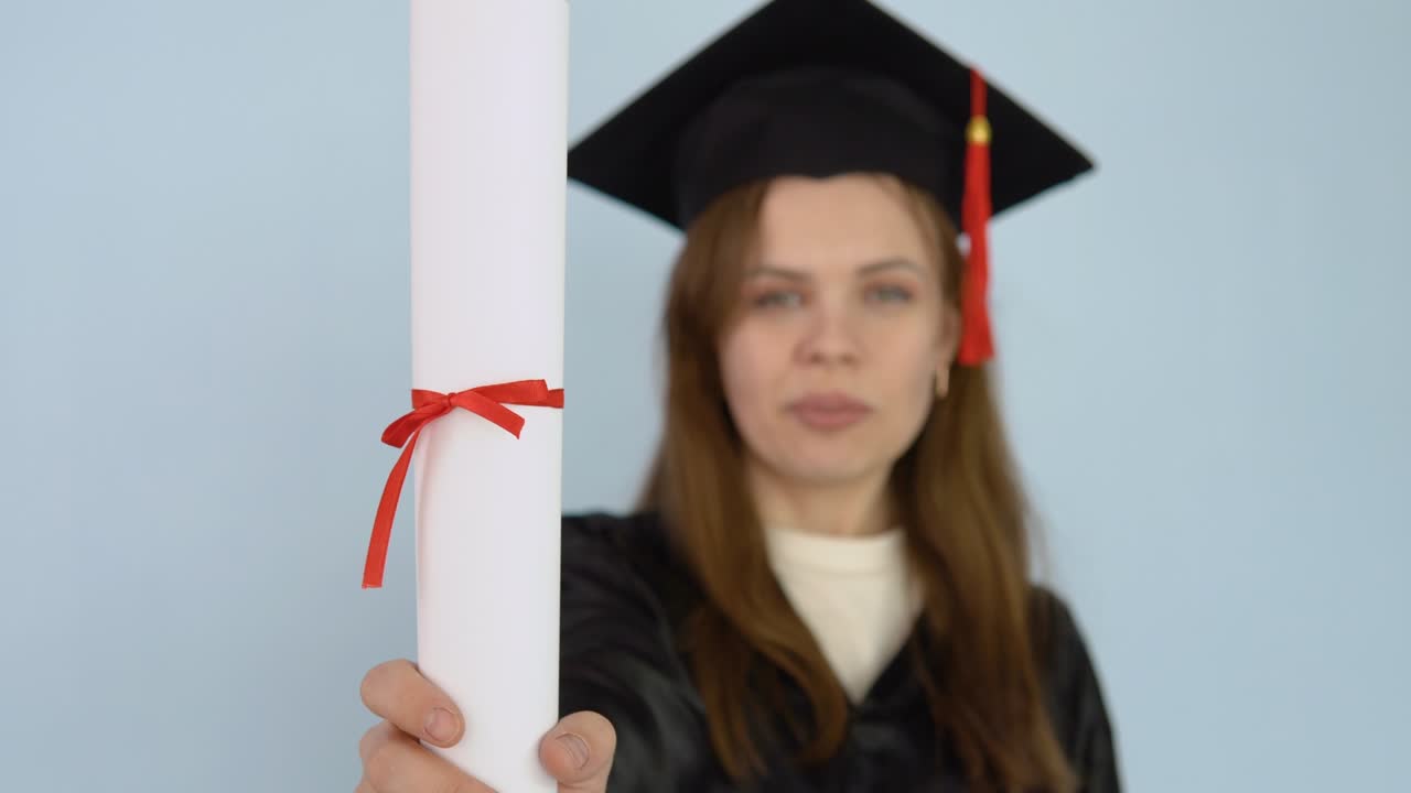 una joven estudiante con una bata negra y un sombrero de maestría sostiene en sus manos en posición vertical un diploma de educación superior. una graduada universitaria baila con un diploma en sus manos y estornuda