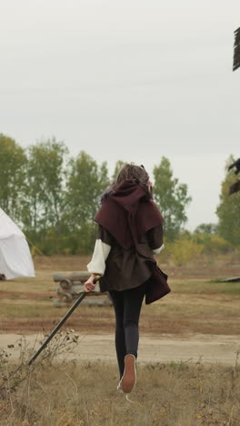 teenage girl rushes home to medieval village after practicing sword fighting. young woman improves fighting skills and physical endurance backside view