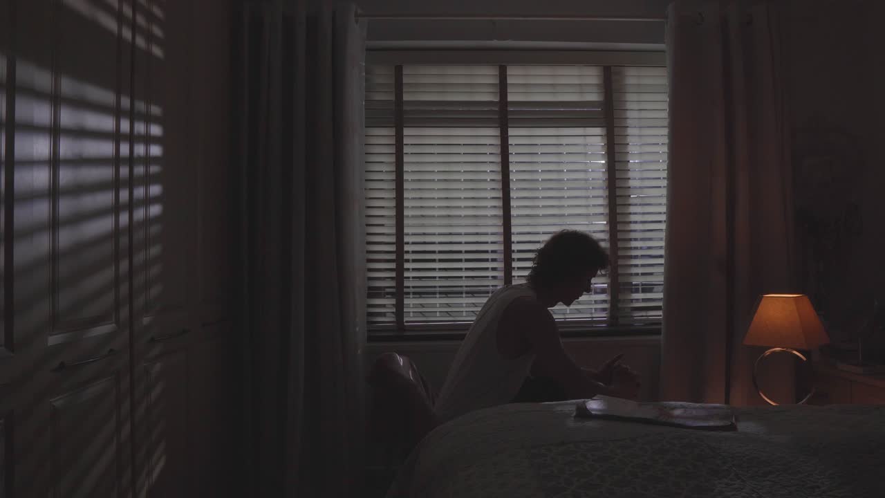 Man remains still as blinds and warm lamp light frame the mood, sadness with struggle