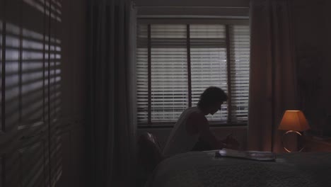 man remains still as blinds and warm lamp light frame the mood, sadness with struggle