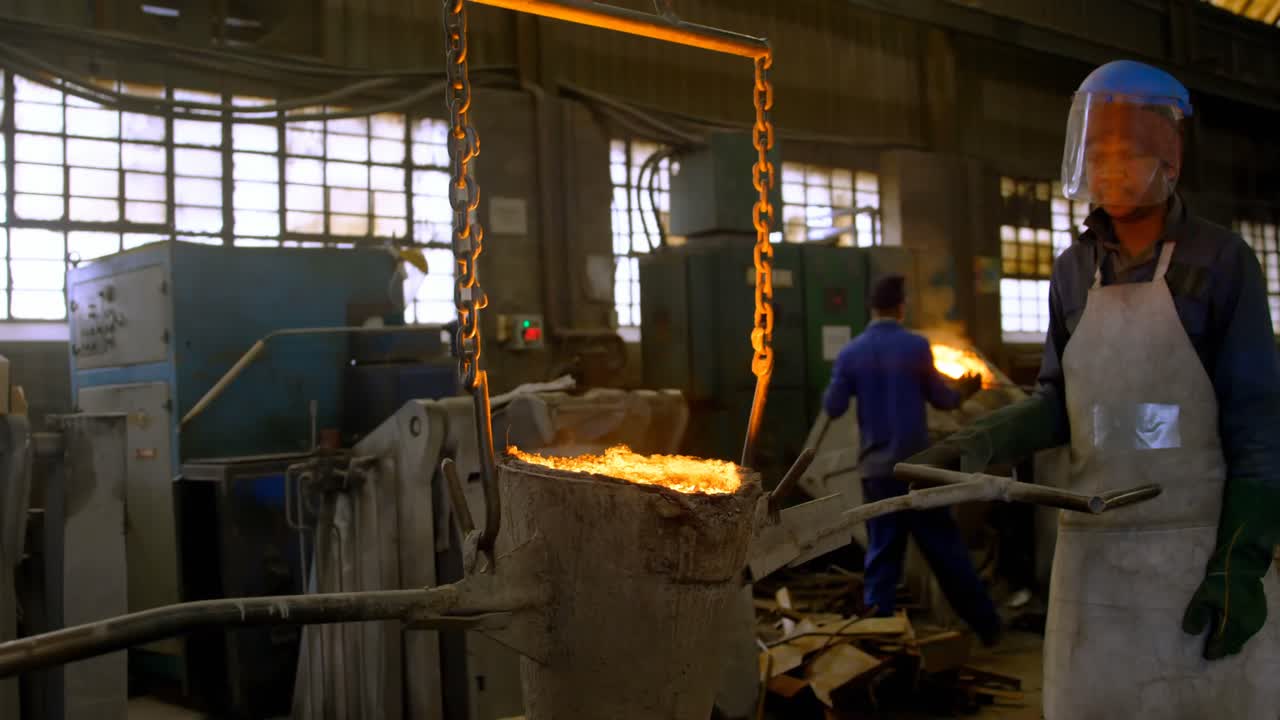 рабочий мужчины, несущий расплавленный металл в мастерской 4k