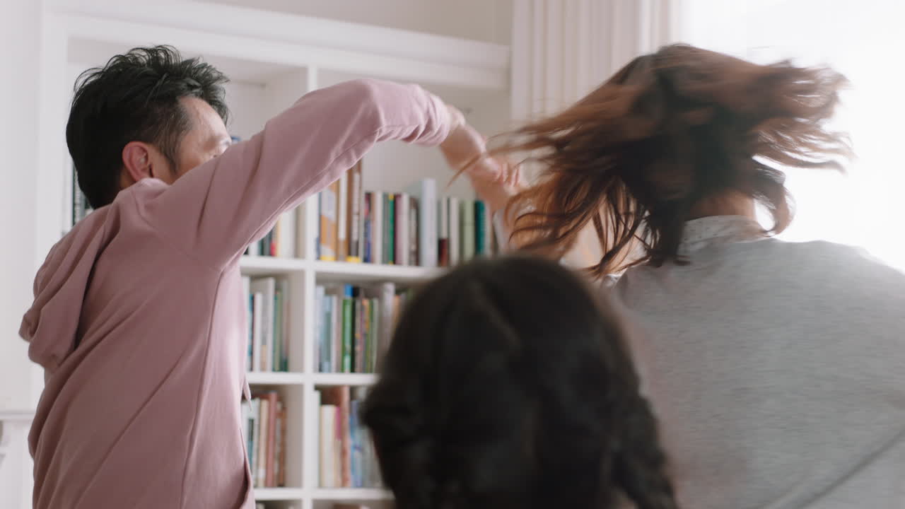 행복한 아시아 가족이 집에서 춤을 추고 즐거운 춤을 추고 함께 축하합니다. 작은 아이들이 엄마와 아빠와 함께 축하하고 흥미진진한 주말 4k 영상을 즐기고 있습니다.