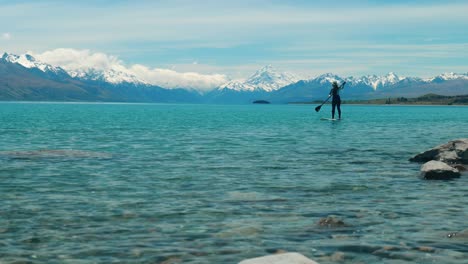 Panorama-De-Aventuras:-Surfista-De-Remo-En-El-Lago,-Monte-Cook-Al-Fondo,-En-Un-Cautivador-Metraje-De-Archivo