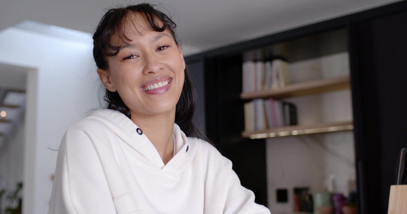 Donna in felpa con cappuccio che nota la telecamera, sorridendo, gesticolando, appoggiando il mento, salutando gli spettatori a casa con il PC