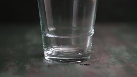 pouring water into a bottom of a glass close-up on the dark background