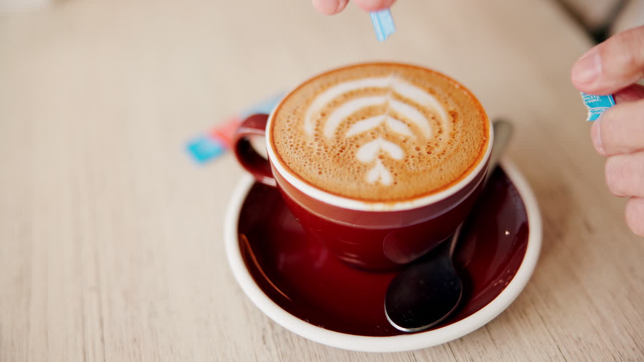 Person adding sugar to a cappuccino with latte art
