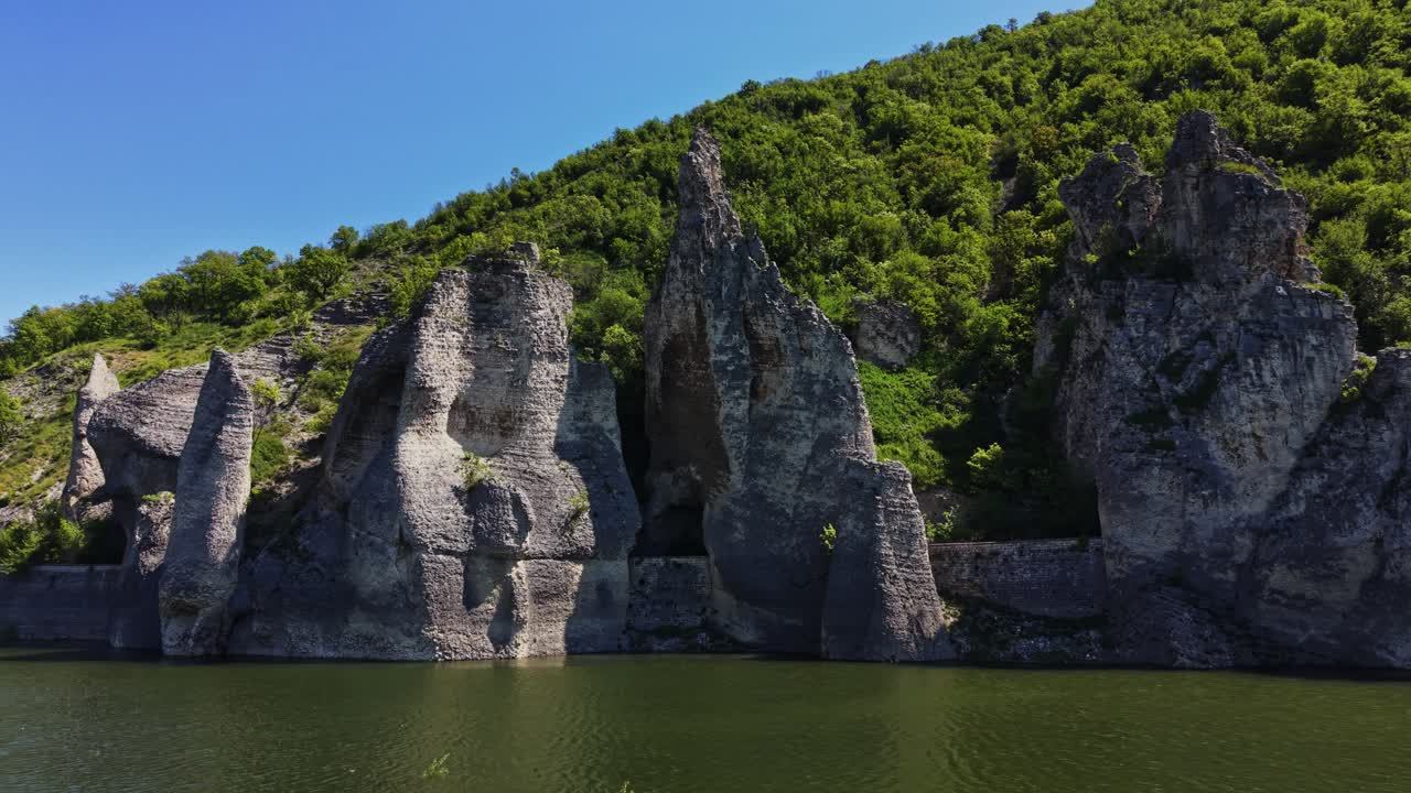 Skalní útvary u vody v zelené krajině za slunečného dne.