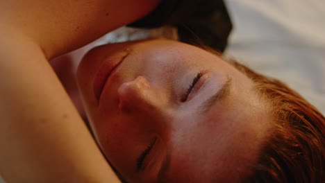 hermosa mujer pelirroja girando la cabeza mientras está acostada en la cama