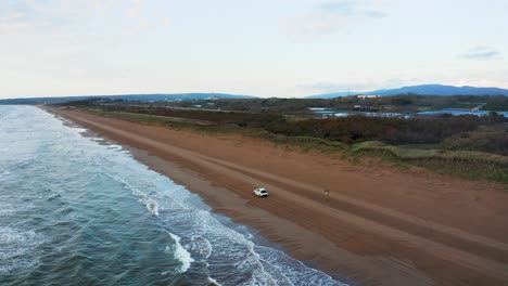 Car-driving-on-Beach,-Aerial-Pan-View,-Ishikawa-Prefecture-Japan