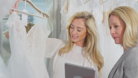 sales assistant with digital tablet helping woman to choose wedding dress in bridal store